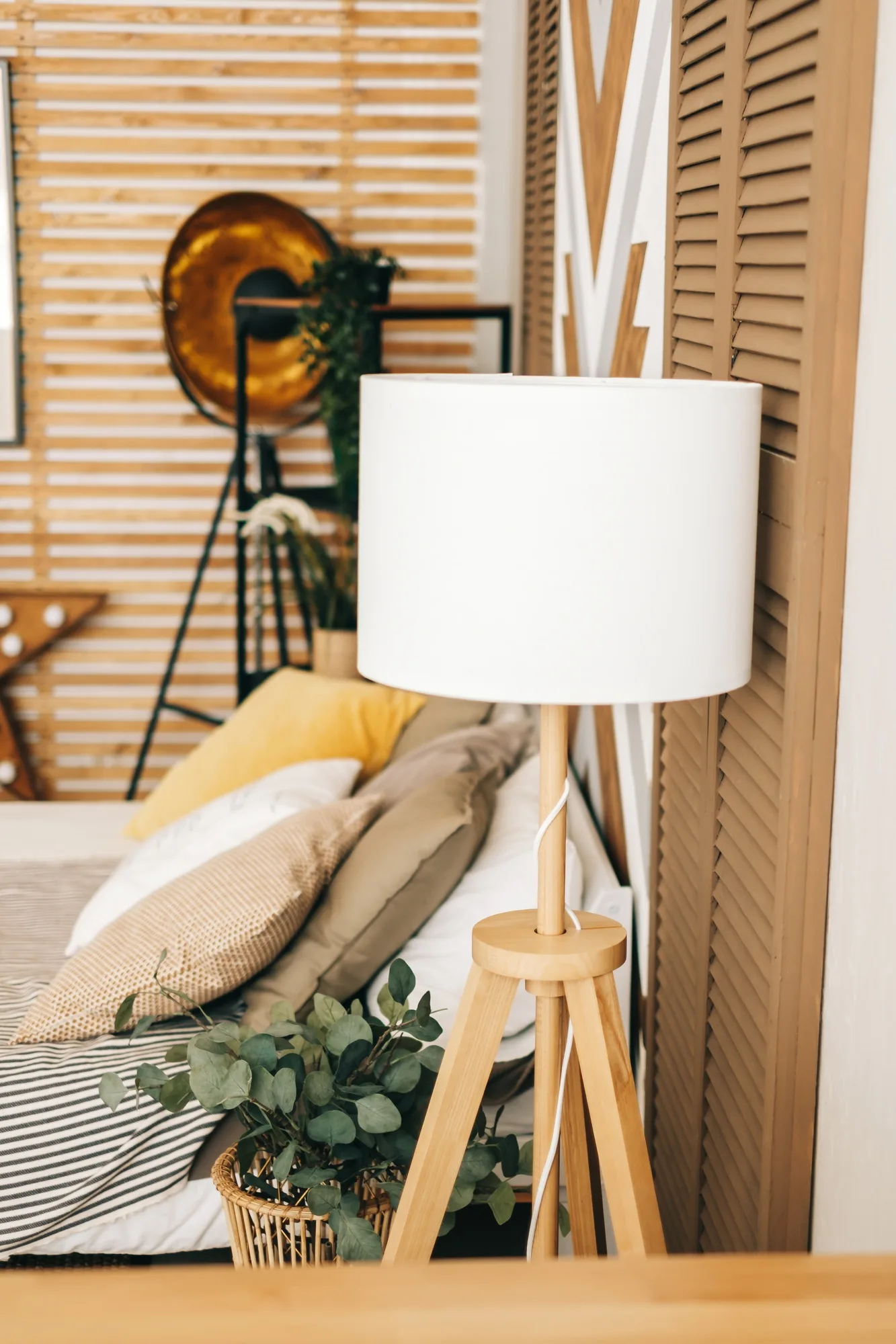 Wooden floor lamp and plants near the bed, interior design detail.